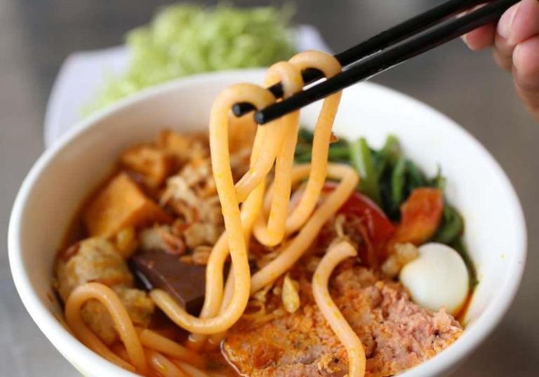 Món bún có màu đỏ đặc trưng từ hạt điều, kết hợp nước lèo đậm đà từ xương heo và gạch cua.